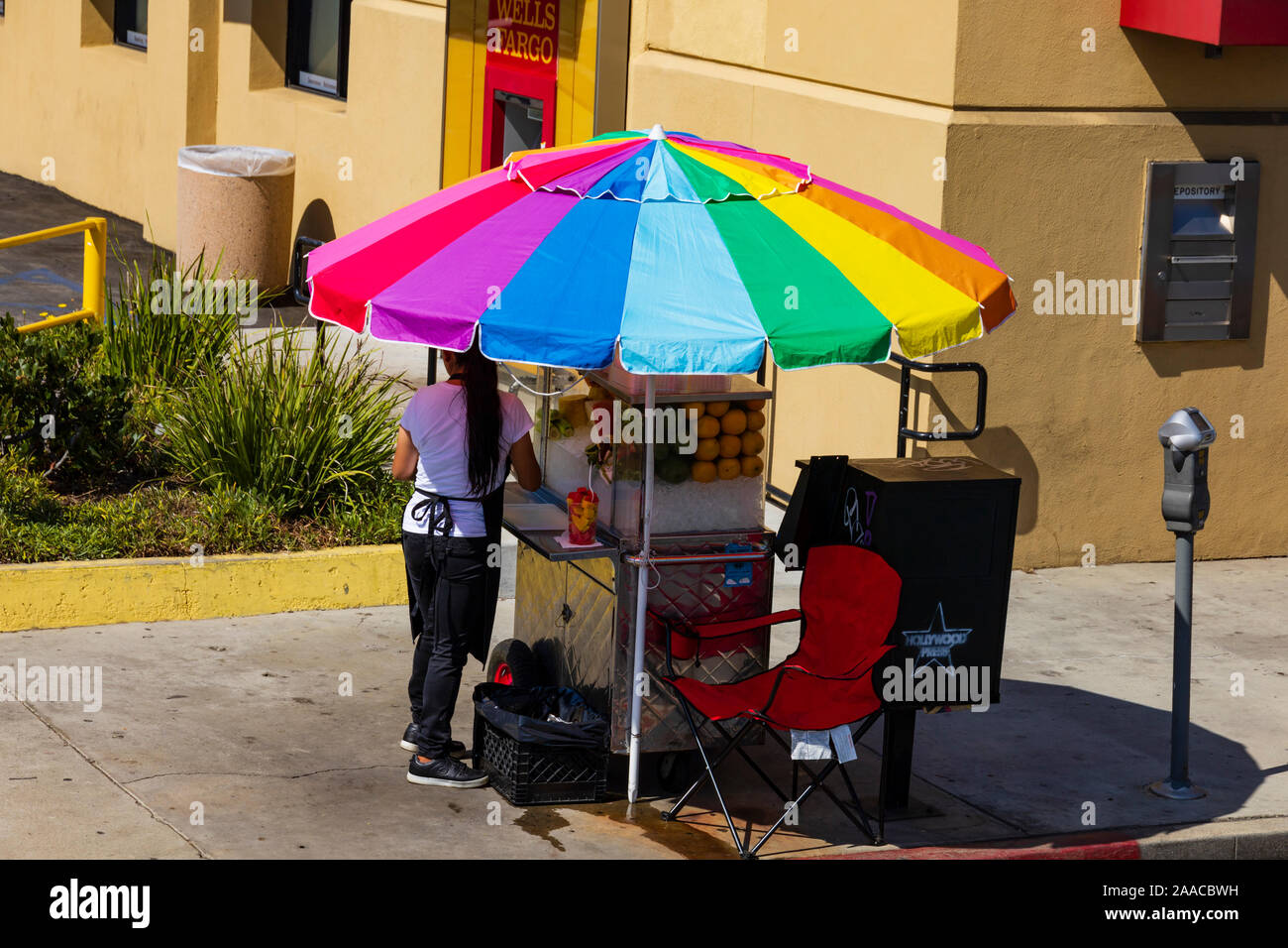 Sidewalk vendor stall with woman selling fruit smoothies under a colourful umbrella. Los Angeles, California, United States of America. Stock Photo