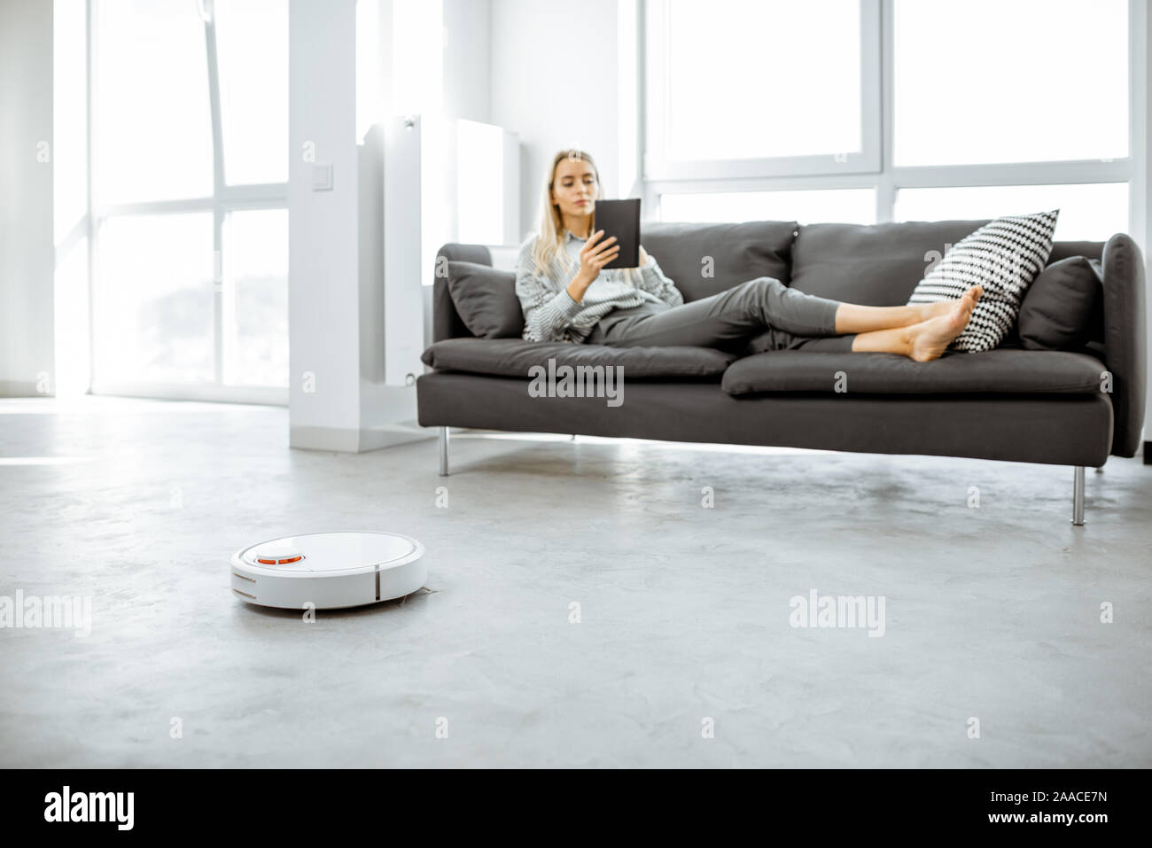 Woman Relaxing On The Couch While Automatic Vacuum Cleaner Doing