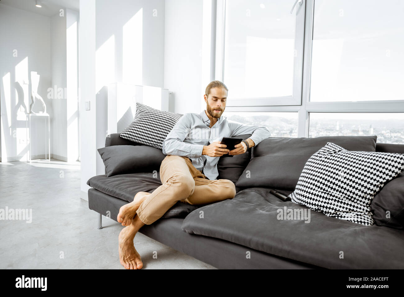 Full length portrait of a handsome caucasian man sitting with digital tablet on the couch in the bright living room Stock Photo