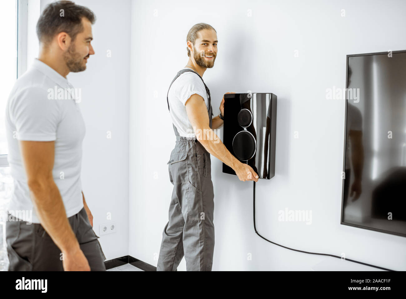 Two professional workmen in workwear installing luxury audio system in the white living room. Home appliances installation concept Stock Photo