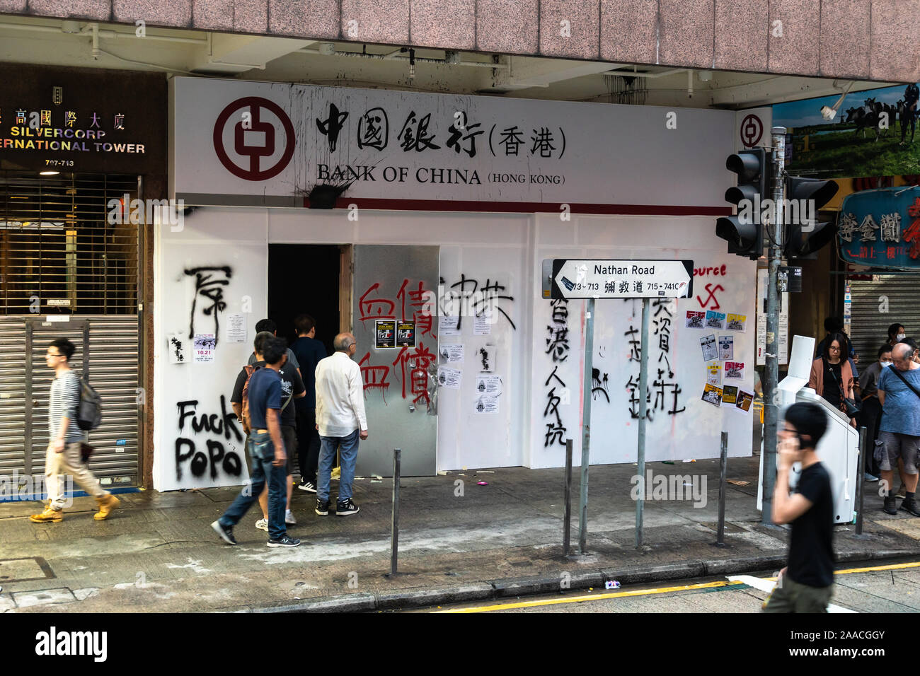 Kowloon, Hong Kong - October 20 2019: People and protestors walk in front of a Chinese bank branch vandalized to protest against the extradition law a Stock Photo