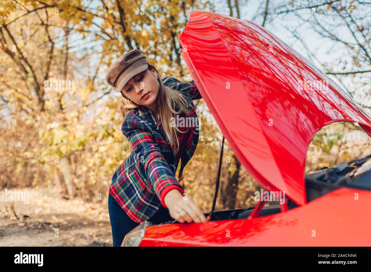 Broken car. Sad woman opening hood of her auto that stopped on forest road outdoors. Breakage Stock Photo