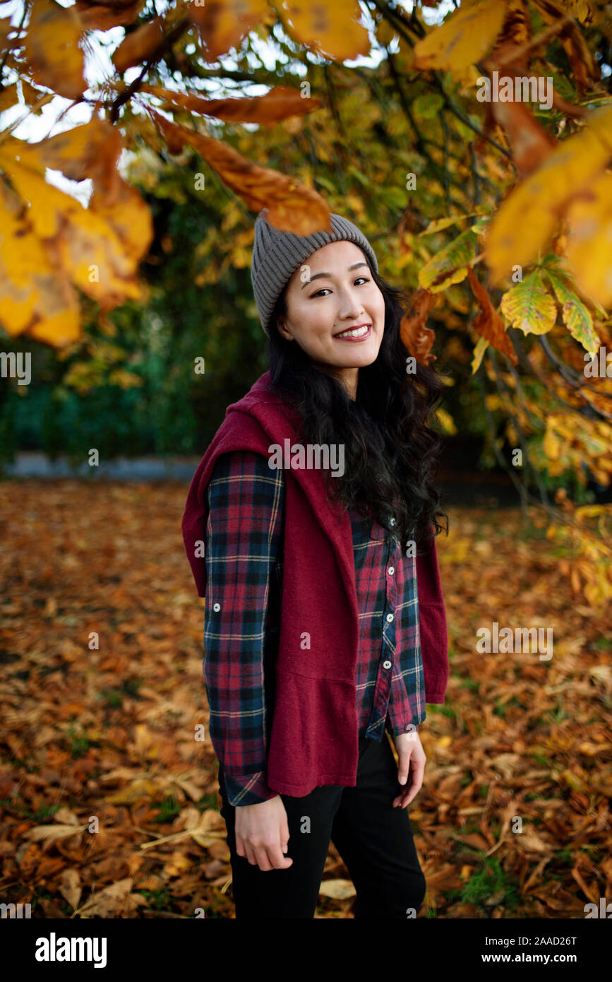 RF Portrait of a smiling Asian (Japanese) female between tree leaves with autumnal colours and student look, MR available. Nov 2019 Stock Photo