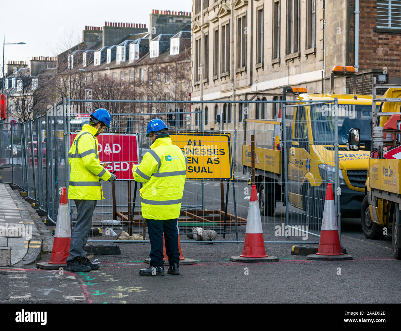 Leith, Edinburgh, Scotland, United Kingdom. 21st Nov, 2019. Trams to Newhaven work starts: Constitution Street is closed to traffic for the next 2-3 years to build the extension for Edinburgh's tram line from to Newhaven, with 8 more stops over 2.91 miles. Barriers are put up along the road. The work is being undertaken by SFN (Sacyr Farrans Neopul) and MUS (Morrison Utility Services). Men with Trams to Newhaven yellow jackets wearing hard hats next to a road closed sign Stock Photo