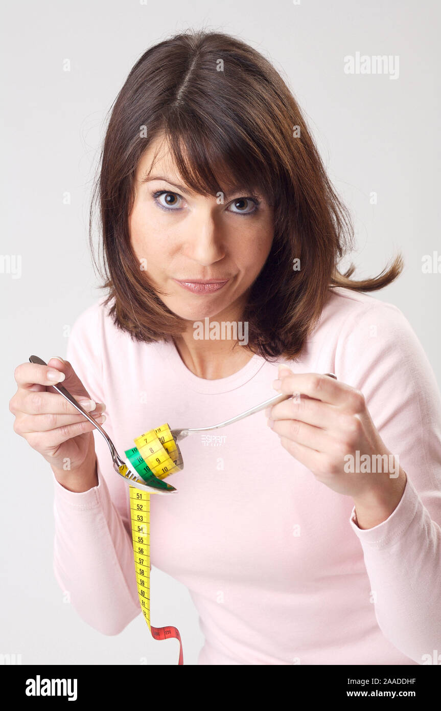 Junge Frau wickelt ein Massband mit Ihrem Essbesteck auf | young woman rolling up a measure tape by using her cutlery Stock Photo