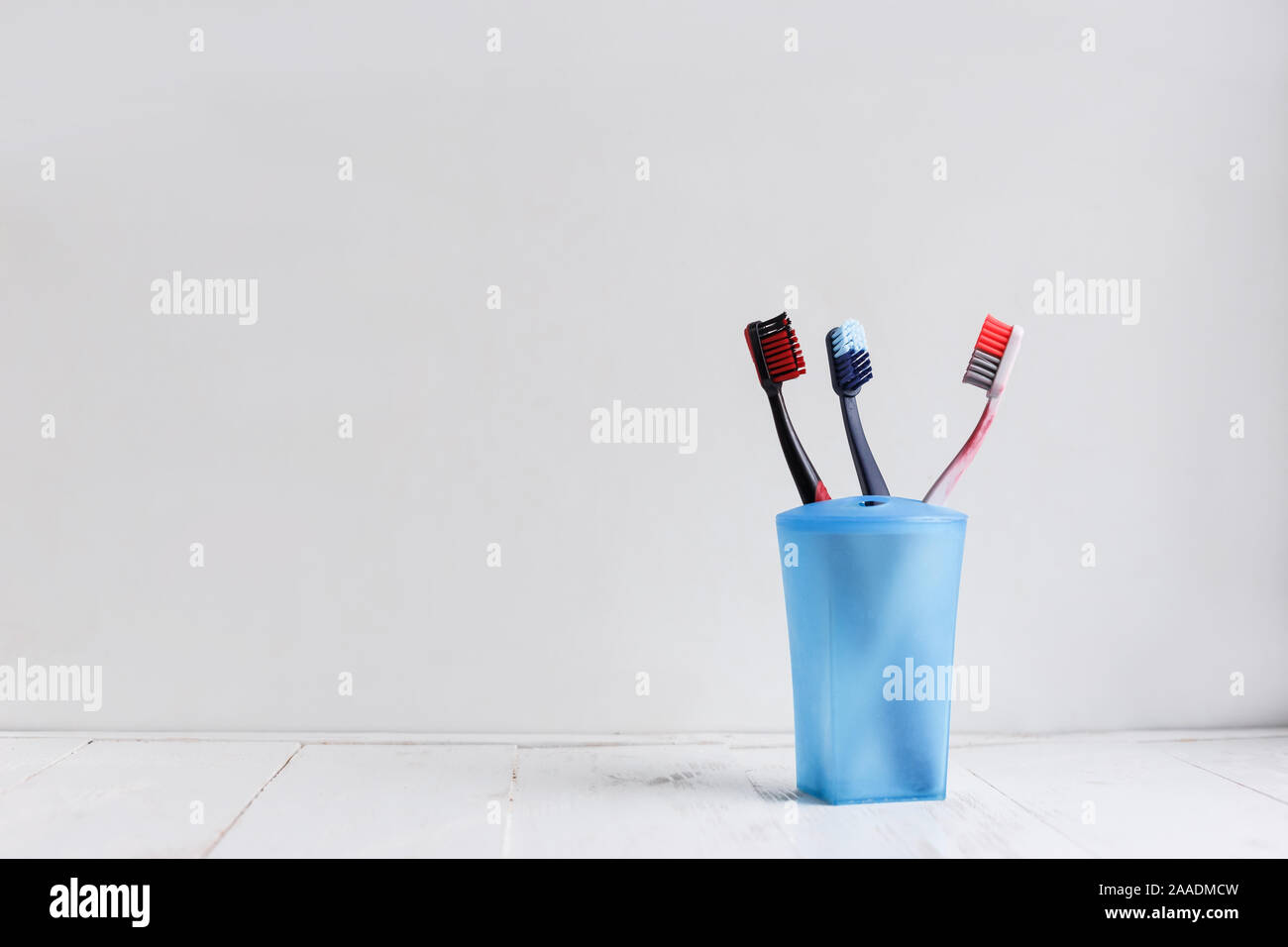 Family toothbrushes in blue cup on white wooden shelf Stock Photo Alamy