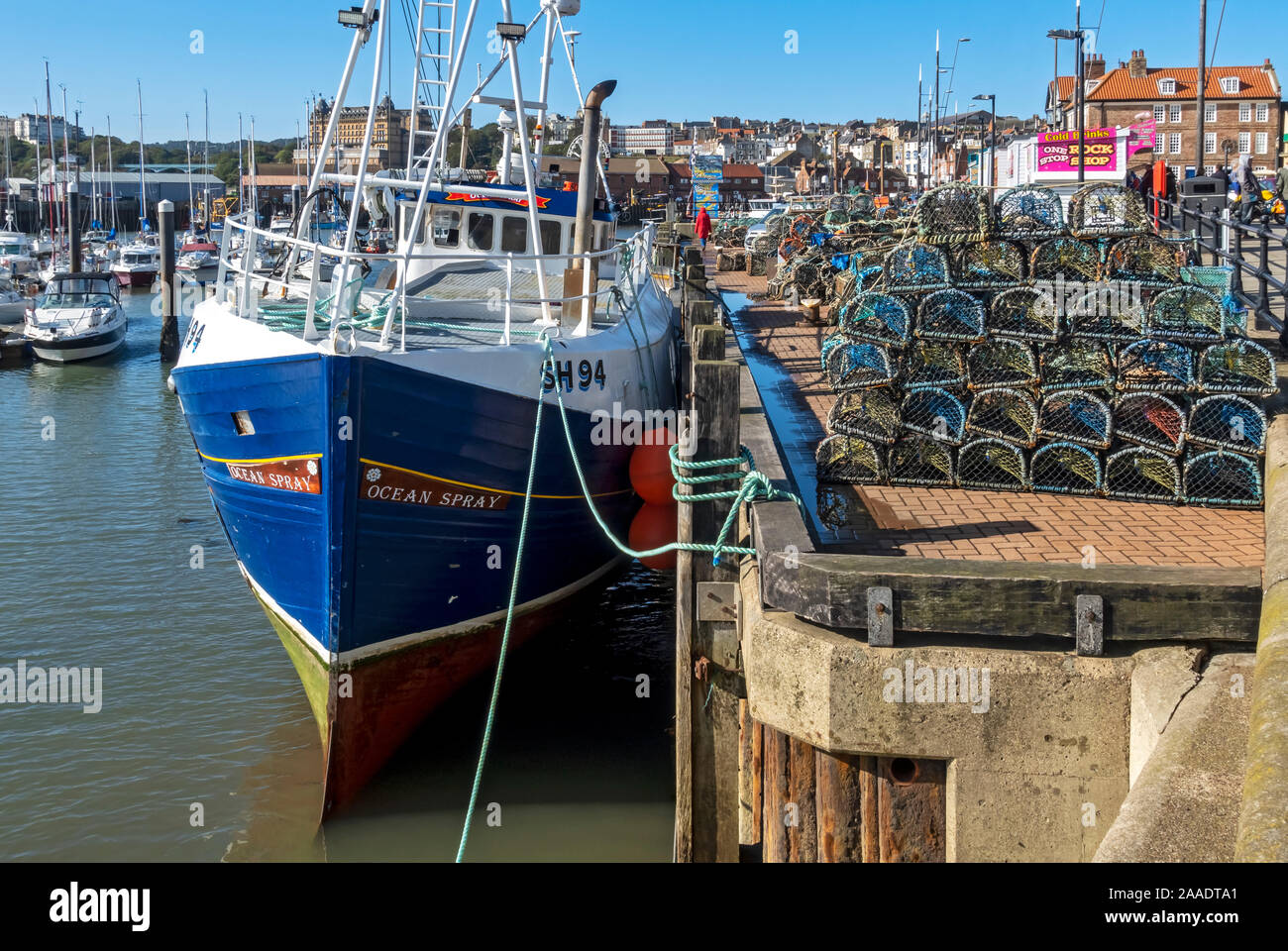 Fishing boat at low tide next to stacks of lobster and crab pots on the quayside Scarborough North Yorkshire England UK United Kingdom GB Britain Stock Photo