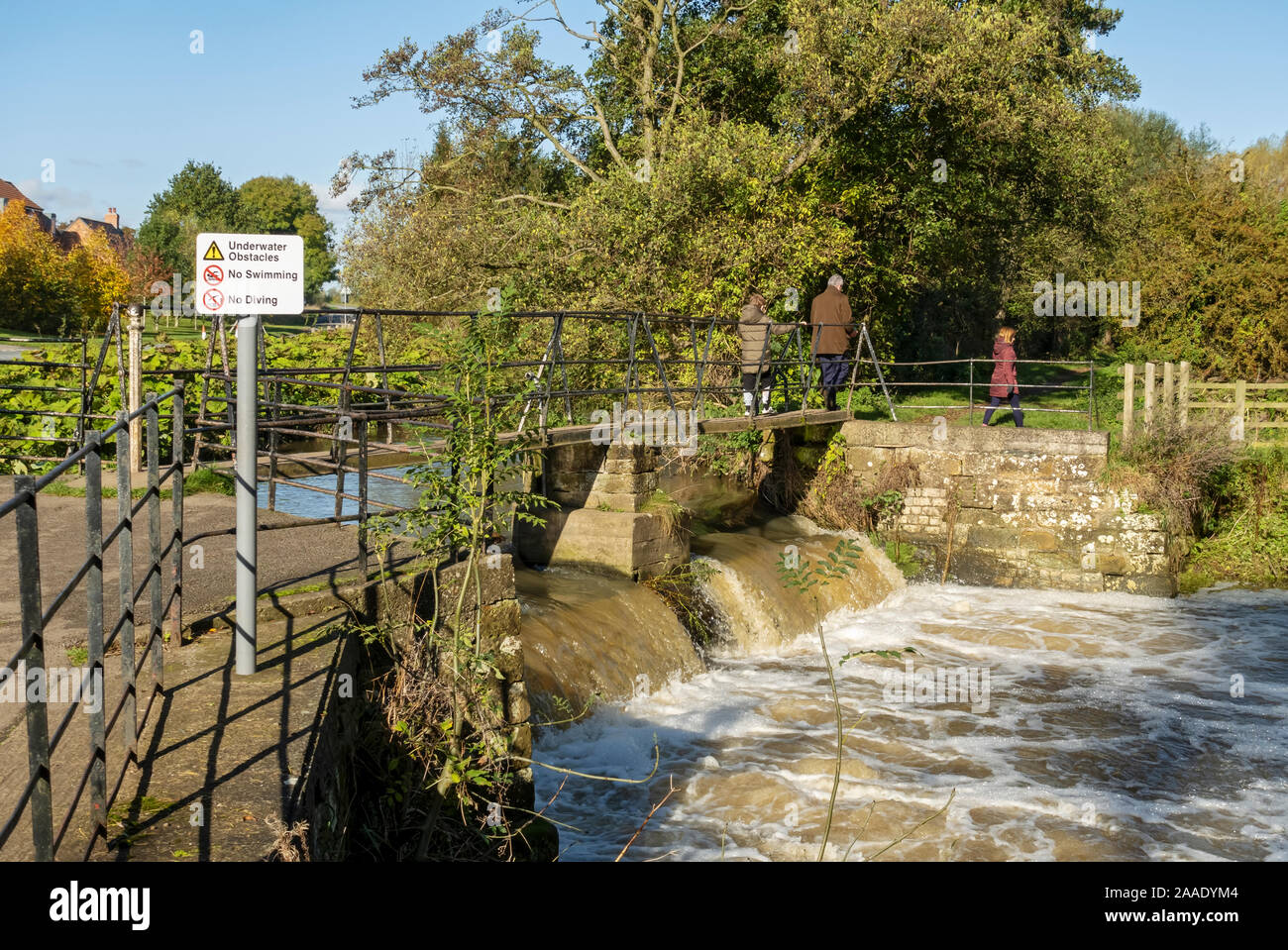 Walkers people crossing the footbridge over the old sluice gates of Thirsk Mill Thirsk North Yorkshire England UK United Kingdom GB Great Britain Stock Photo