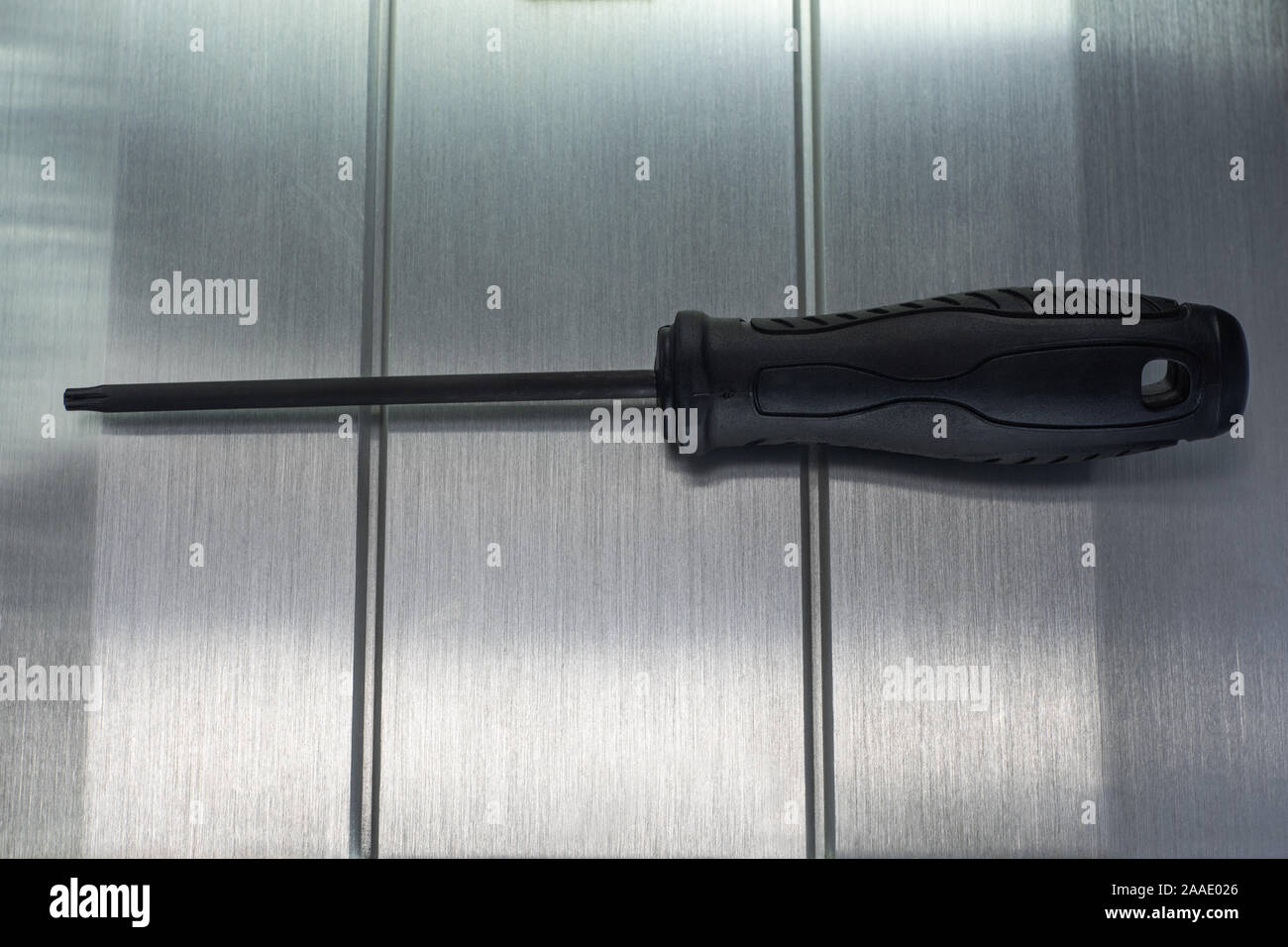 Professional reinforced black matt screw driver placed on a polished aluminum surface. View from the top. Stock Photo