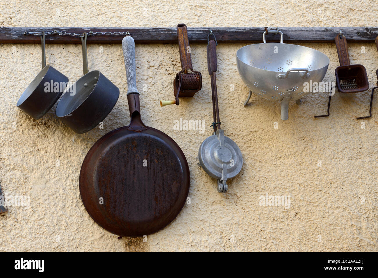 Vintage or Antique Collection of Old Kitchen Utensils Hanging on Wall Rack including Pans, Drainers & Spatulas Stock Photo