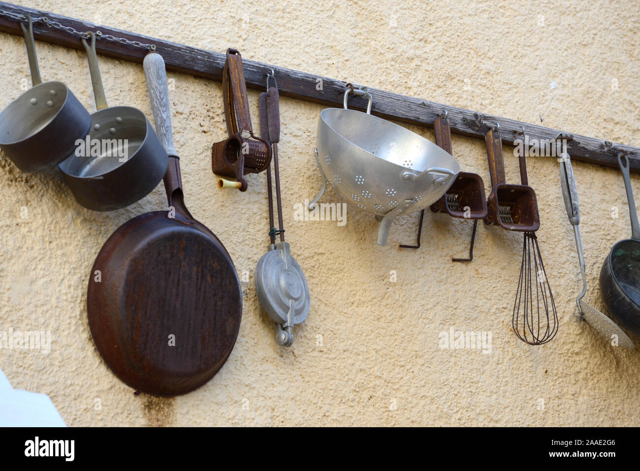 Vintage or Antique Collection of Old Kitchen Utensils Hanging on Wall Rack including Pans, Drainers & Spatulas Stock Photo