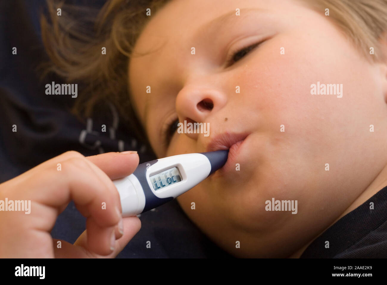 siebenjähriger Junge liegt im Bett mit Fieberthermometer im Mund (MR) Stock Photo
