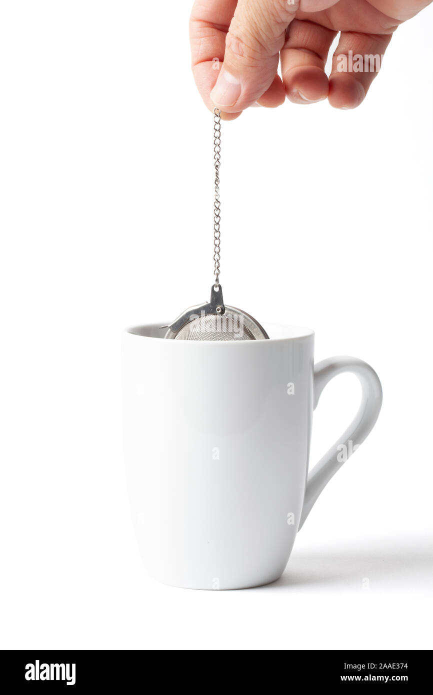 Metallic tea strainer infuser in a human hand immersing and soaking in a cup isolated on white Stock Photo