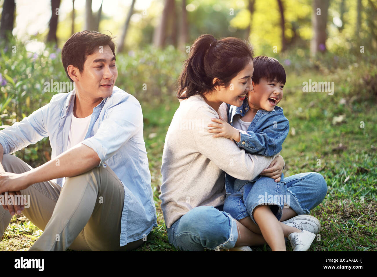 asian family mother father and son sitting on grass relaxing having fun outdoors in park Stock Photo