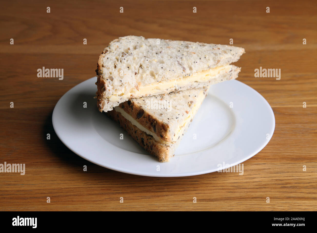 A Plain Cheese Sandwich served with multigrain bread cut in half on white plate on wooden dinner table Stock Photo