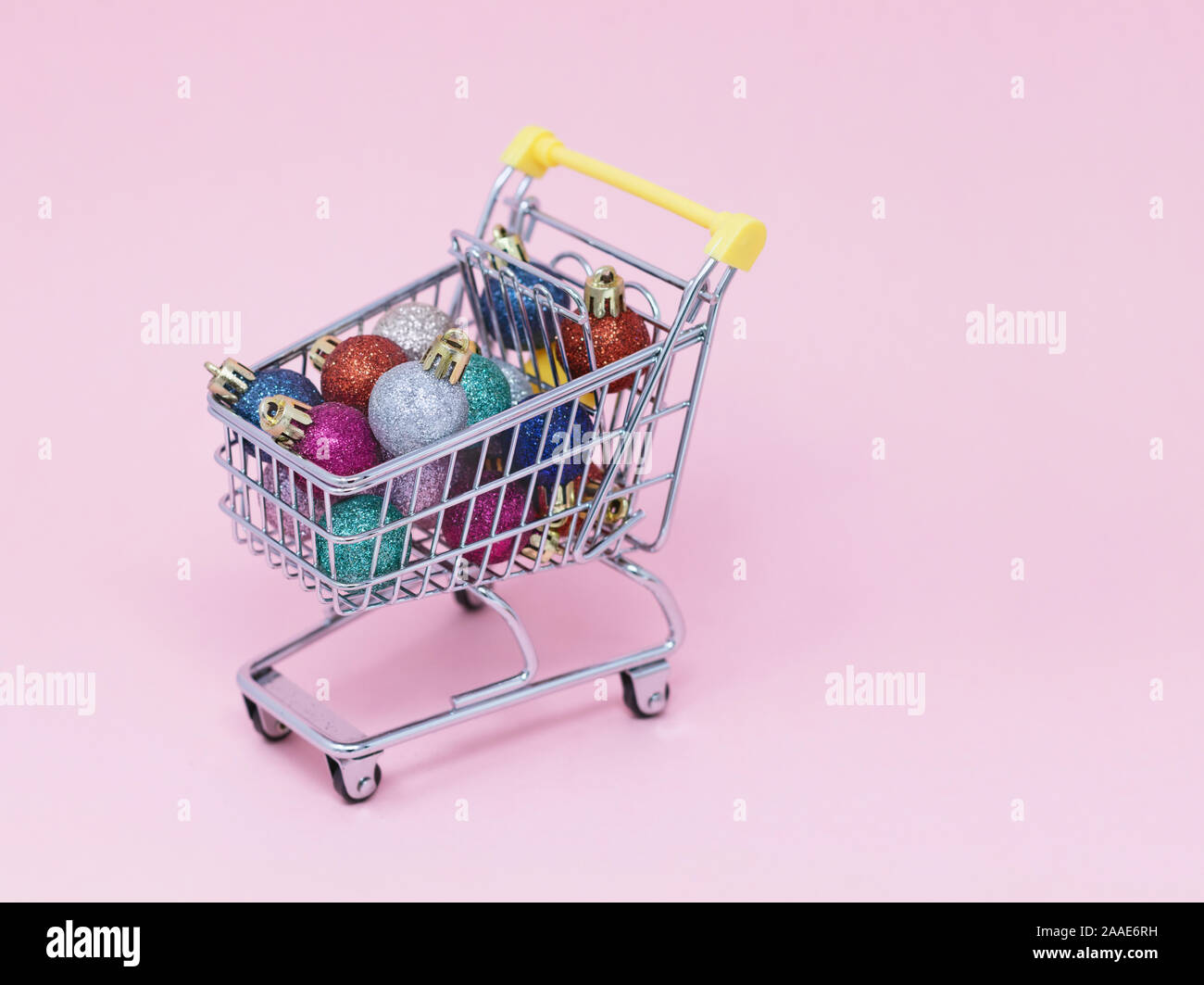 Christmas shopping composition, Trolley filled with sparkly baubles on a pink background Stock Photo