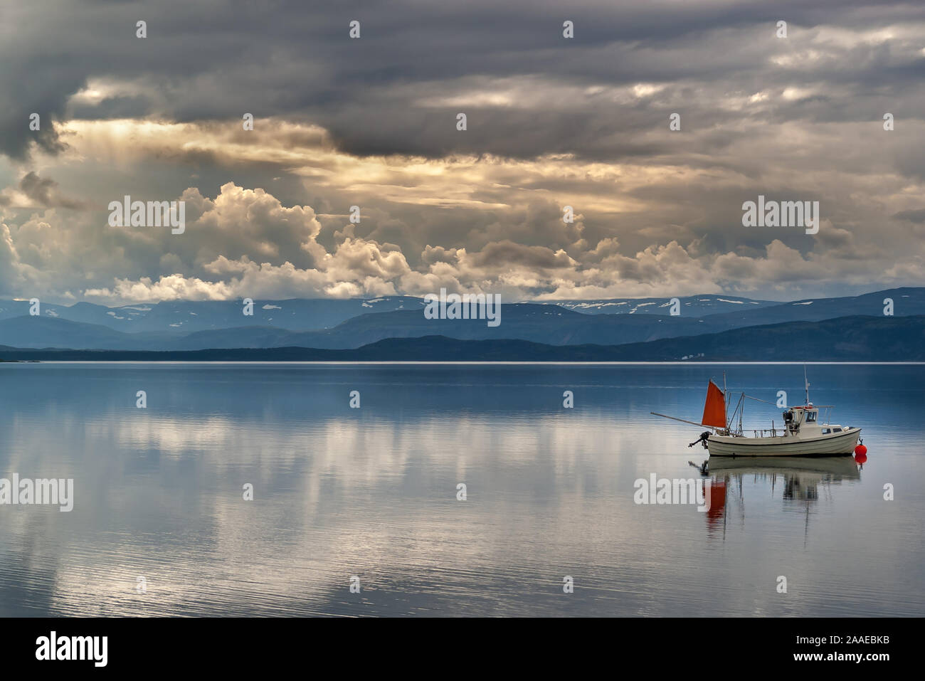 A summer landscape of the Barents Sea near the Norwegian coast (Porsanger Fjord) with a fishing boat in calm sea water, cloudy sky and mountains. Stock Photo