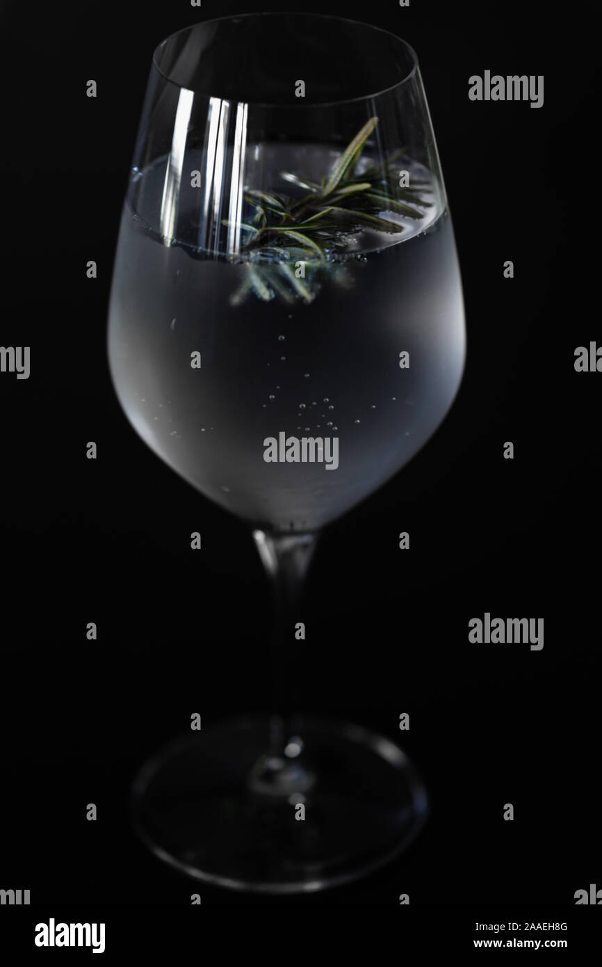 Closeup of a Wine glass with ice cold Gin Tonic with a twig of rosemary for the flavor, isolated before a black background. Stock Photo