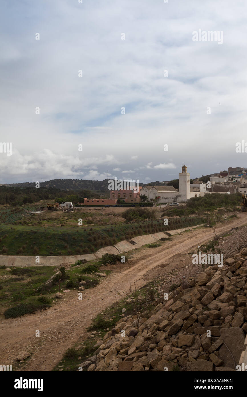Construction of a new road. Green autumn nature. Small village Diabat with a mosque. Mountains in the background. Cloudy early evening sky. Diabat (Es Stock Photo