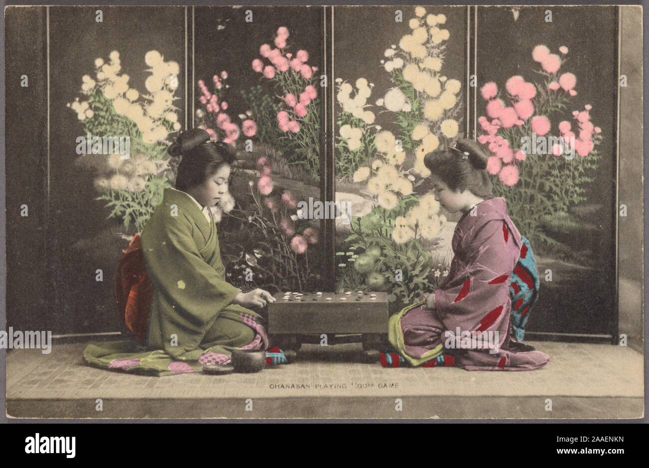 Illustrated postcard of two Japanese women (o-hana-san), wearing traditional Japanese kimono, kneeling on the floor playing the board game called go, with a floral screen behind them, Japan, 1920. From the New York Public Library. () Stock Photo