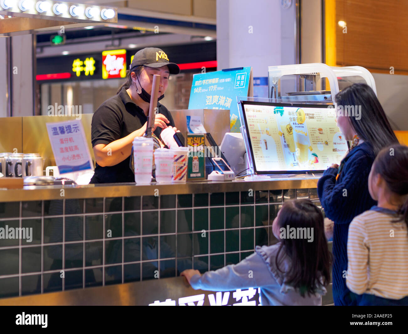 TIANJIN, CHINA - 7 OCT 2019 - A mother of two young children orders drinks from a bubble tea stall within a shopping mall. Food & beverage / consumer Stock Photo