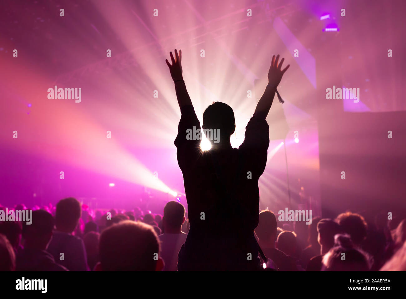 Silhouette of a Woman Dancing Whilst Sat On Someones Shoulders at a Music Concert with Bright Magenta Lighting Stock Photo