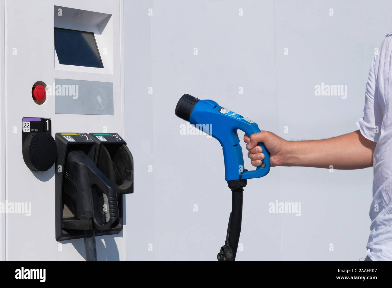 Hand of driver is holding charger for electric cars. Electric charging station. Eco friendly transport concept. Stock Photo