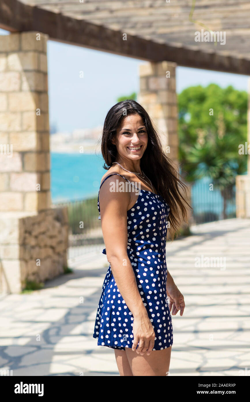 Beautiful smiling woman in blue dress standing outdoors while looking camera Stock Photo