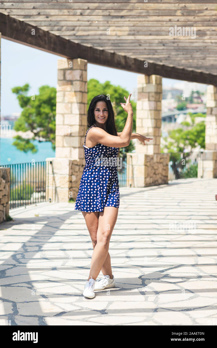 Beautiful smiling woman in blue dress standing outdoors while looking camera Stock Photo