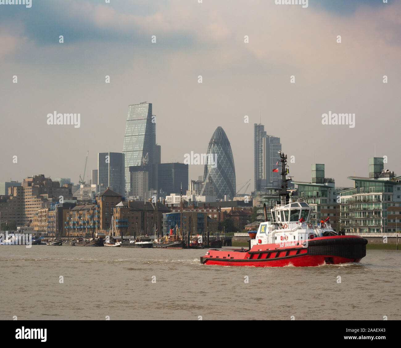 Red and white tugboat SD Shark sails downriver past the City Of London skyline on the river Thames. Stock Photo