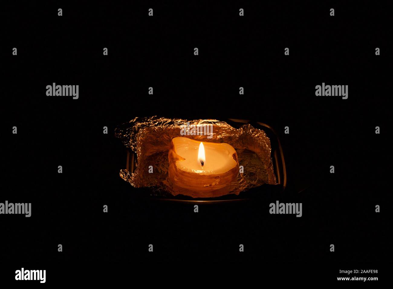 Lit one candle at home darkness after midnight at night into aluminum foil isolated in black background Stock Photo