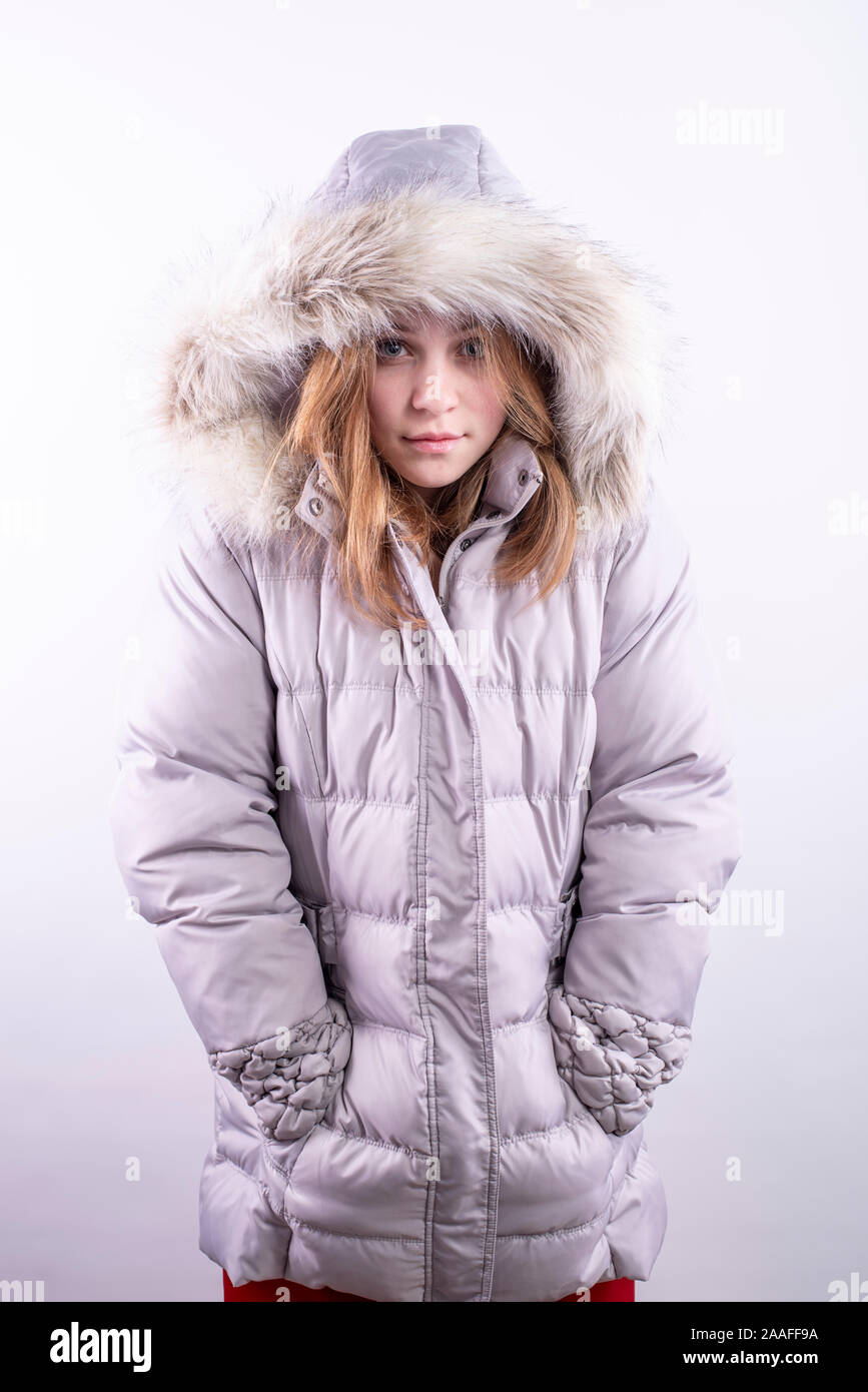 Caucasian teenage girl wearing a silver winter parka with fur-lined hood  and hands in pockets against a white background, vertical orientation Stock  Photo - Alamy