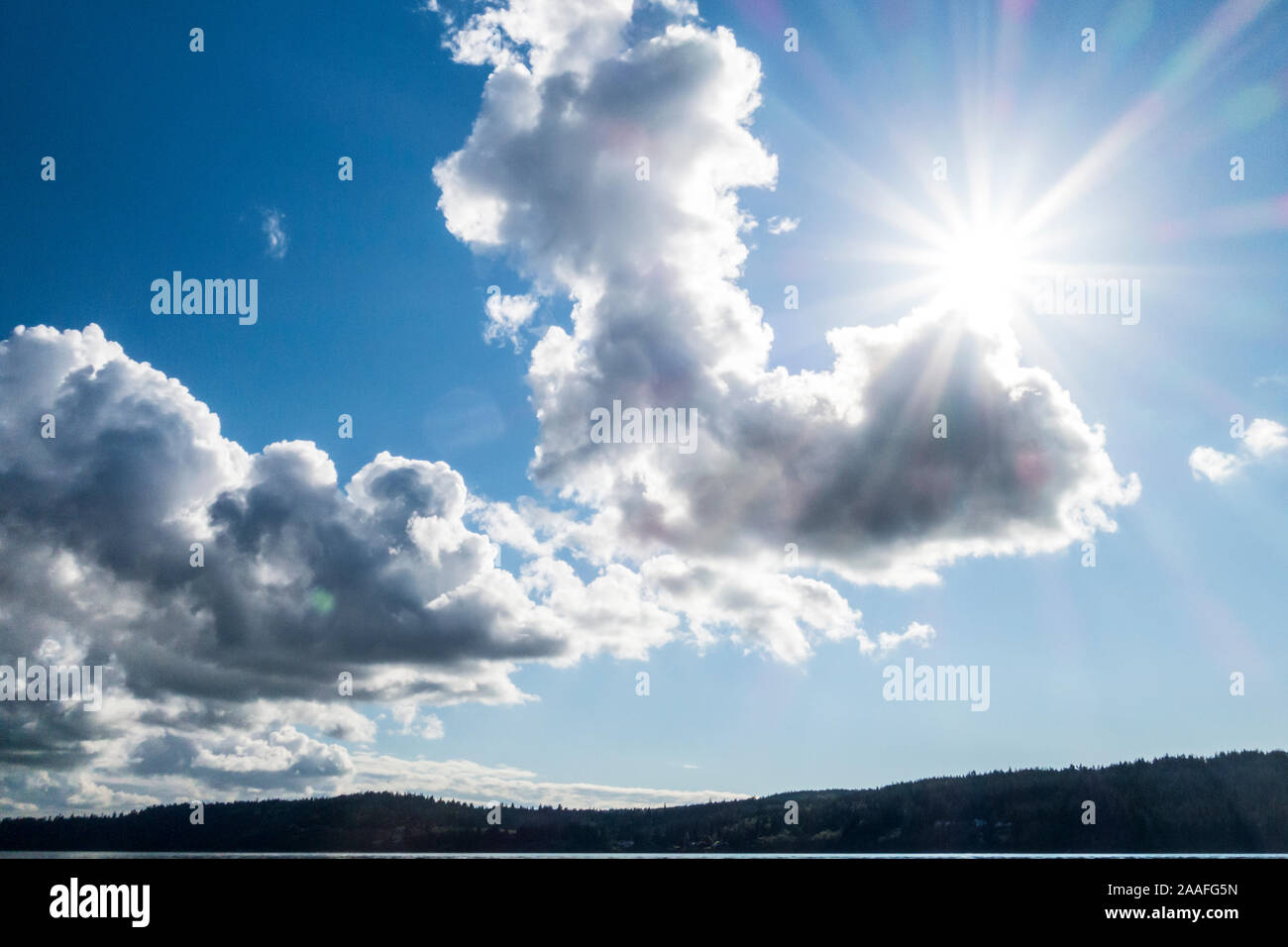 The sun peaking over some white puffy clouds over Whidbey Island, Washington, USA. Stock Photo