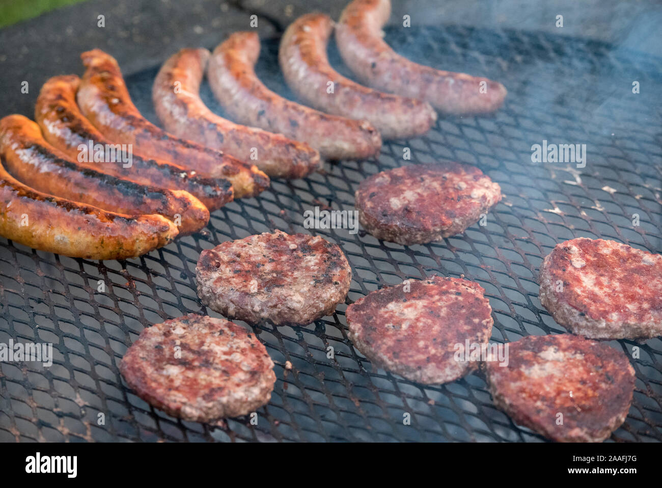 Hamburger patties and sausages being cooked over an open grill Stock