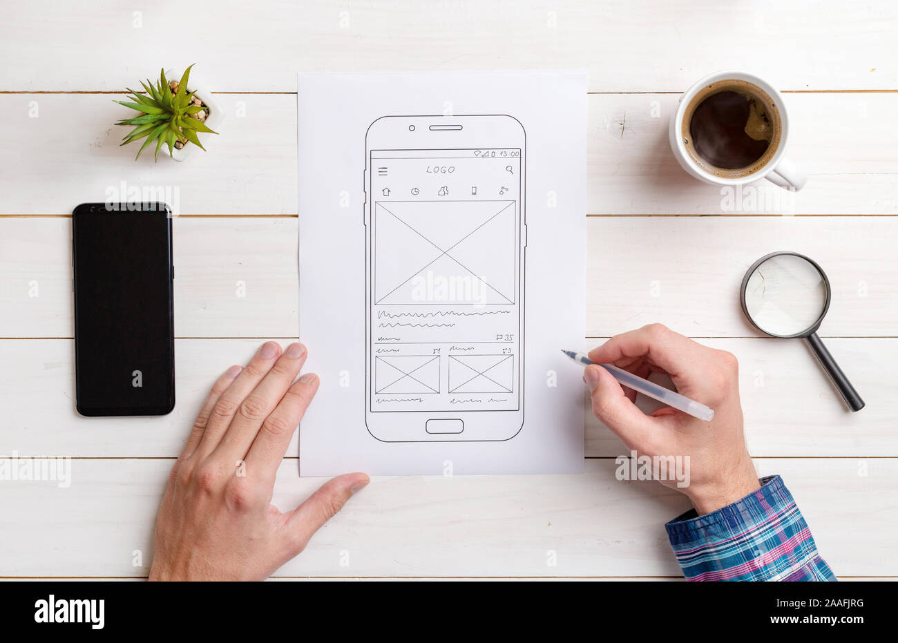 The web designer sketches the user interface on the wireframe of the mobile phone. Work desk, top view, flat lay comosition. Stock Photo