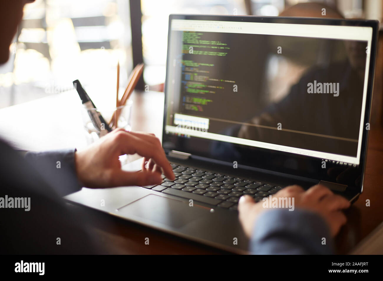 Back view over the shoulder shot of developer programmer with laptop. Program code and script data on the screen. Young freelancer in glasses working Stock Photo