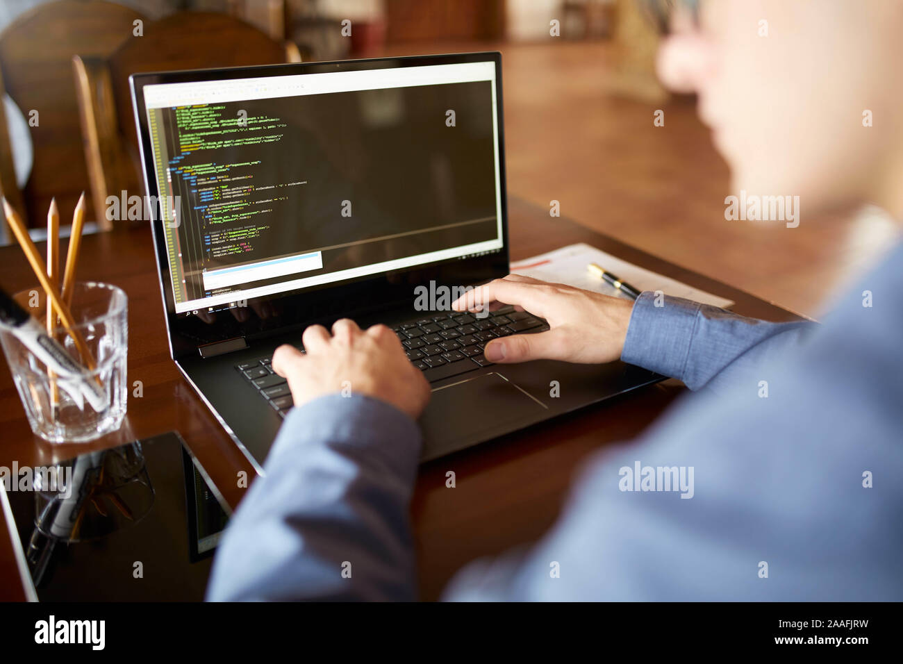 Back view over the shoulder shot of developer programmer with laptop. Program code and script data on the screen. Young freelancer in glasses working Stock Photo
