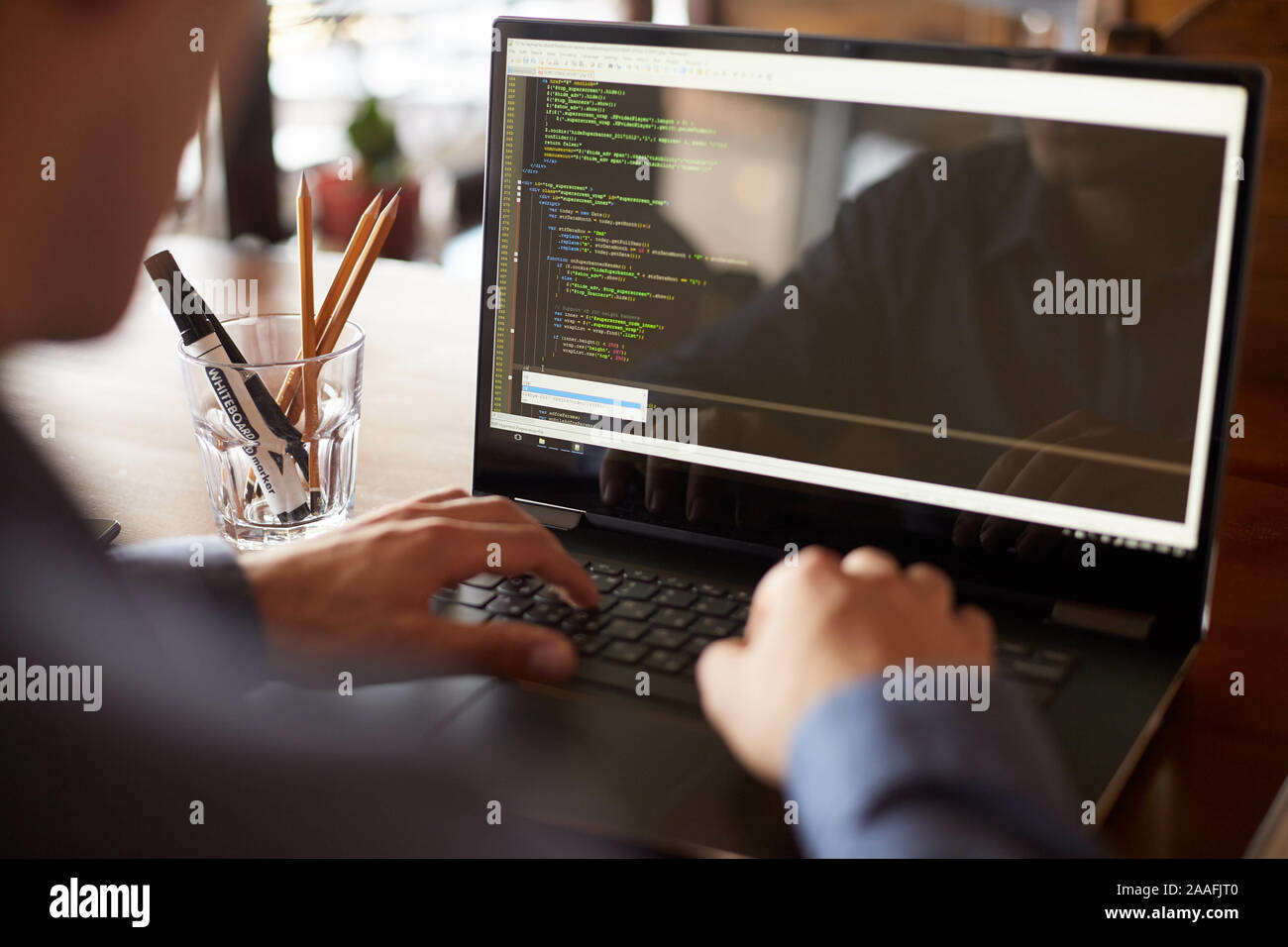 Back view over the shoulder shot of developer programmer with laptop. Program code and script data on the screen. Young freelancer in glasses working Stock Photo