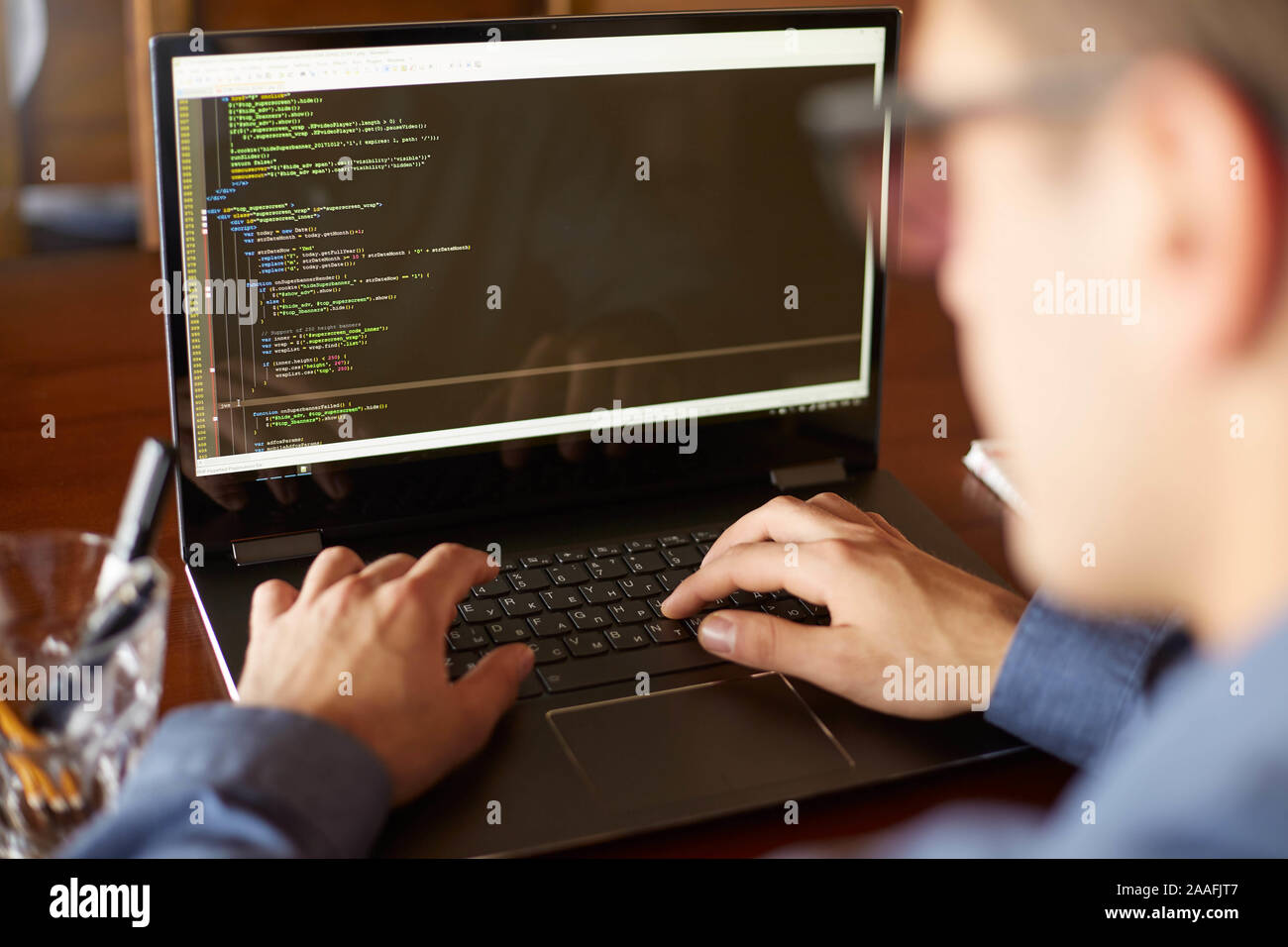 Back view over the shoulder shot of developer programmer with laptop. Program code and script data on the screen. Young freelancer in glasses working Stock Photo