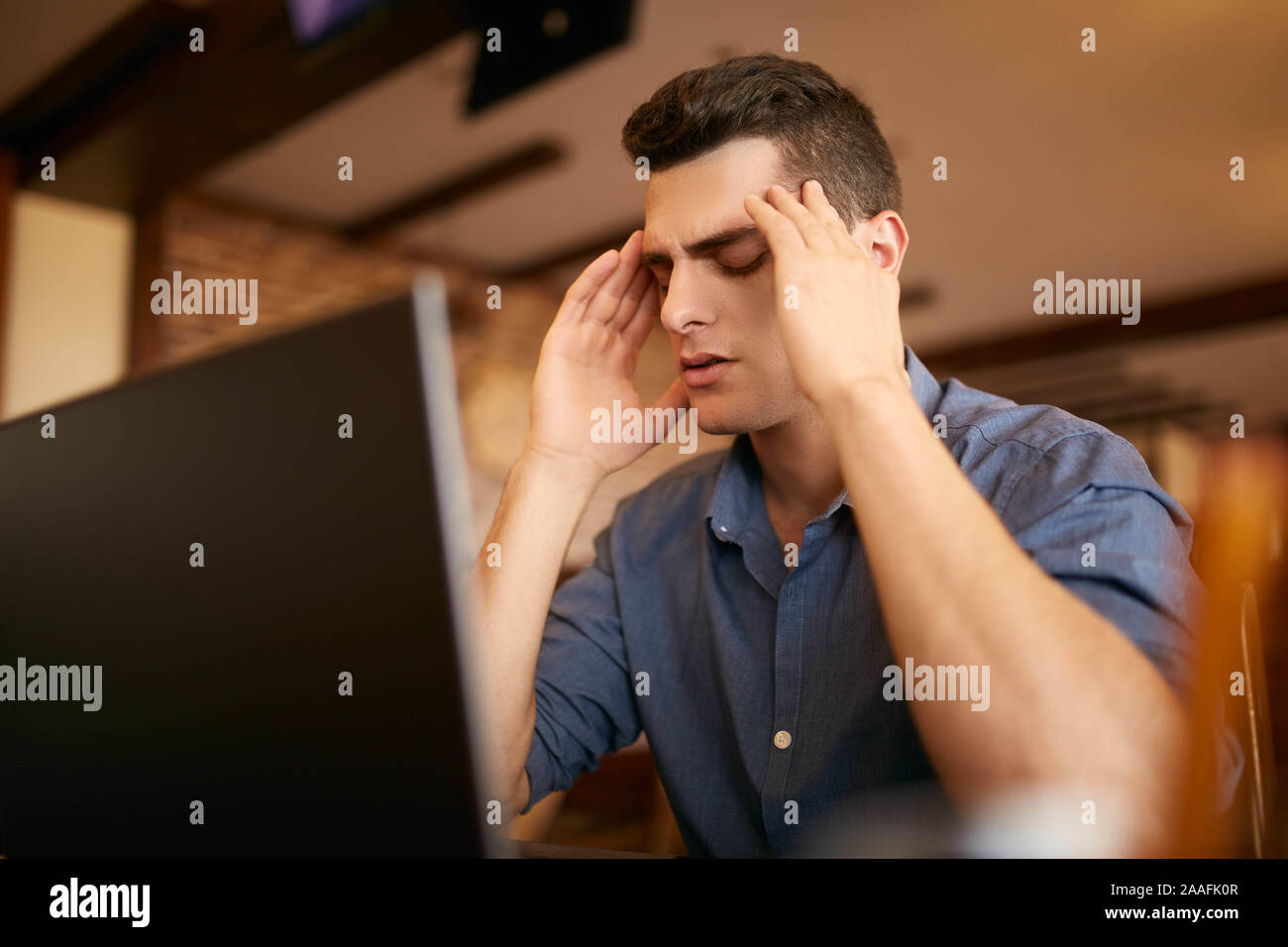 Serious frustrated businessman with closed eyes suffering from headache migraine at workplace, massaging temples. Feeling tired exhausted. Chronic Stock Photo