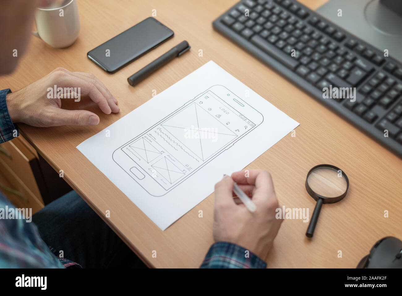 The designer sketches, draws the layout of a mobile phone app on a wireframe. Stock Photo