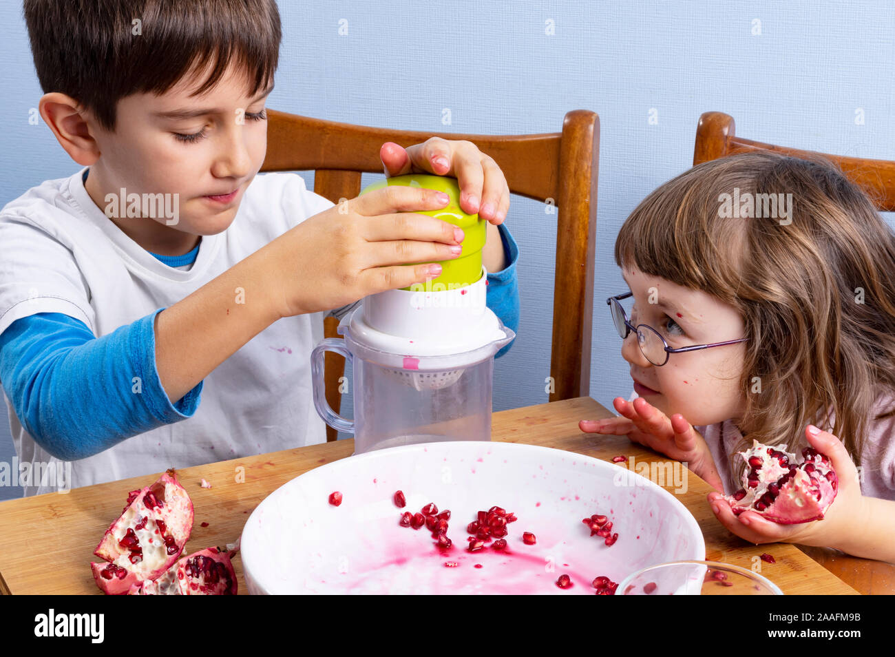 Young boy and girl siblings squeeze pomegranate juice, making a mess. Face and clothes dirty with red spots. Healthy food concept. Stock Photo