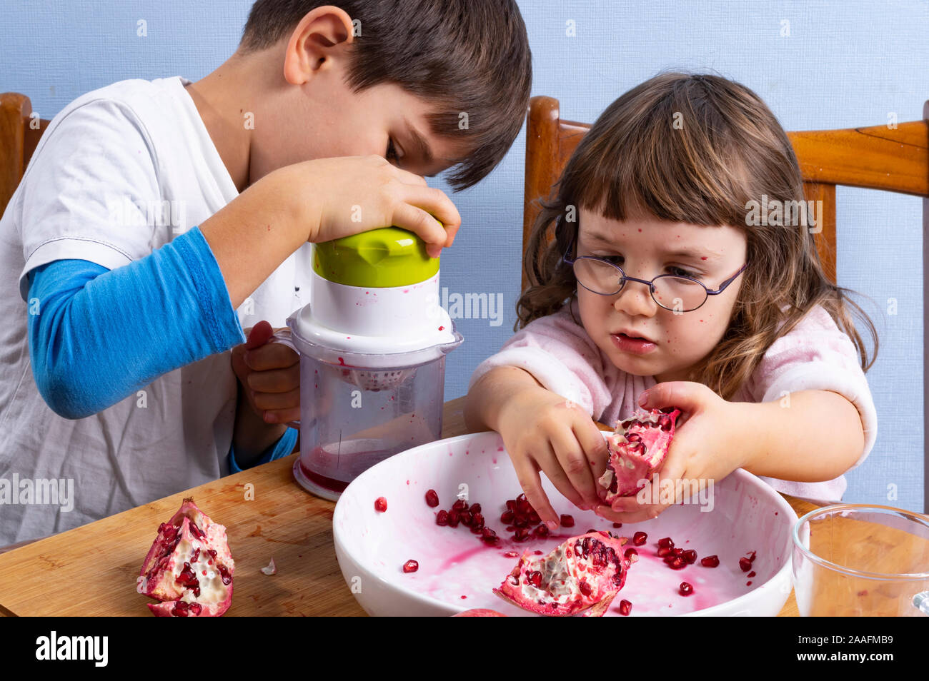 Young boy and girl siblings squeeze pomegranate juice, making a mess. Face and clothes dirty with red spots. Healthy food concept. Stock Photo