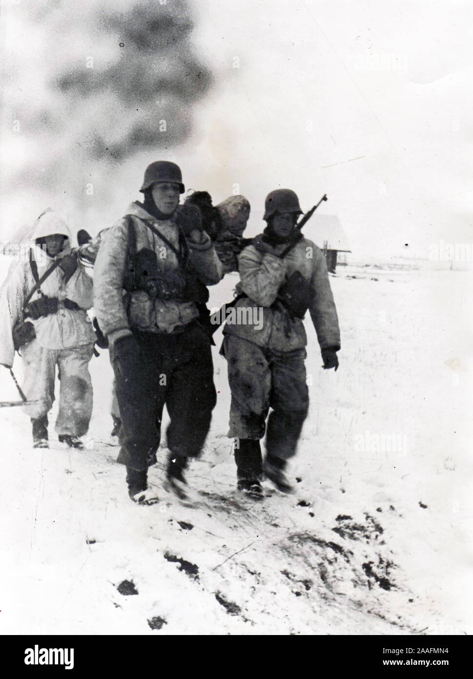 German Soldiers in Snow Camo carry a wounded comrade back from Front 1944 World War Two B/W Press Photo from German origin Stock Photo