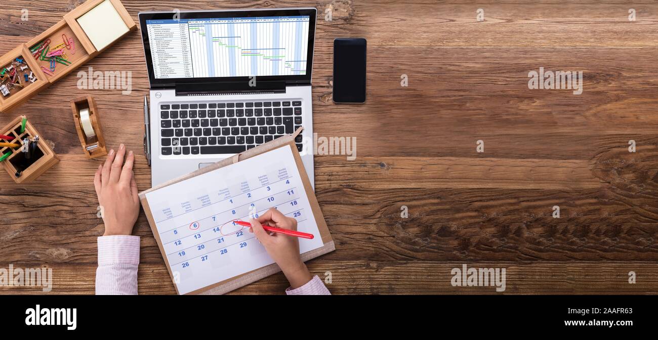 An Overhead View Of Businesswoman Marking Date On Calendar With Gantt Chart On Laptop Screen Stock Photo