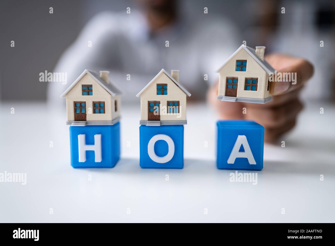 Businesswoman's Hand Placing House Models On Red HOA Cubic Blocks Over Desk Stock Photo