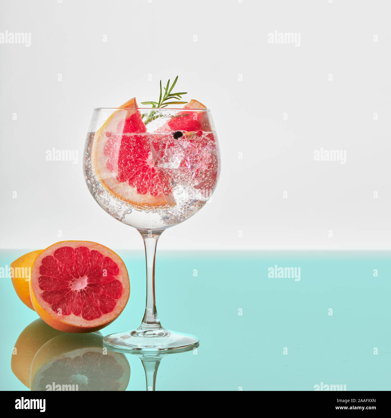 A glass of gin and tonic with slices of grapefruit, green rosemary, ice