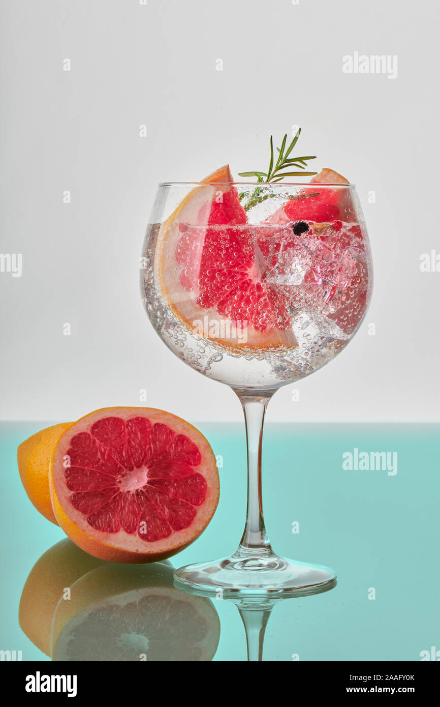 A glass of gin and tonic with slices of grapefruit, green rosemary, ice