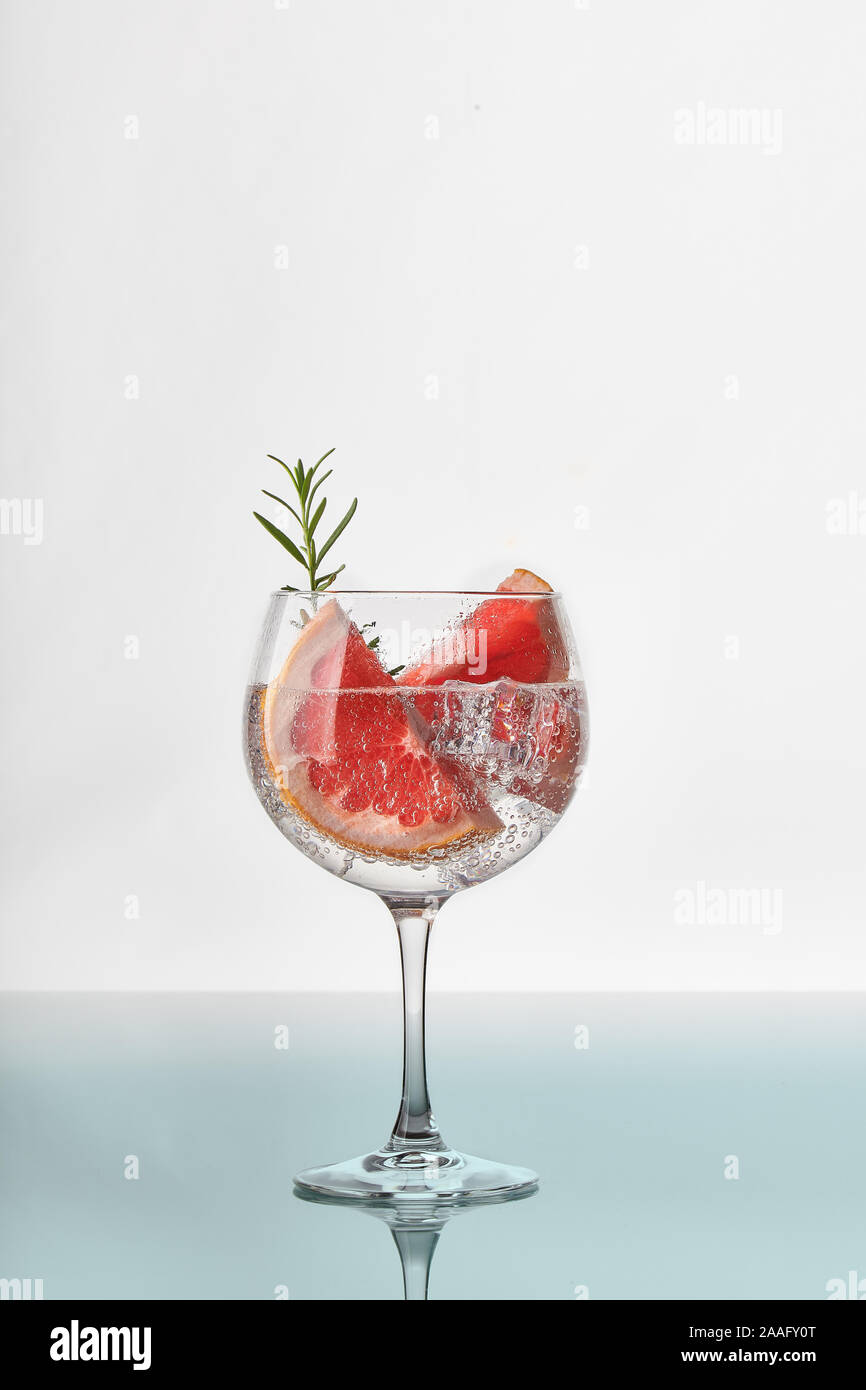 A glass of gin and tonic with slices of grapefruit, green rosemary, ice