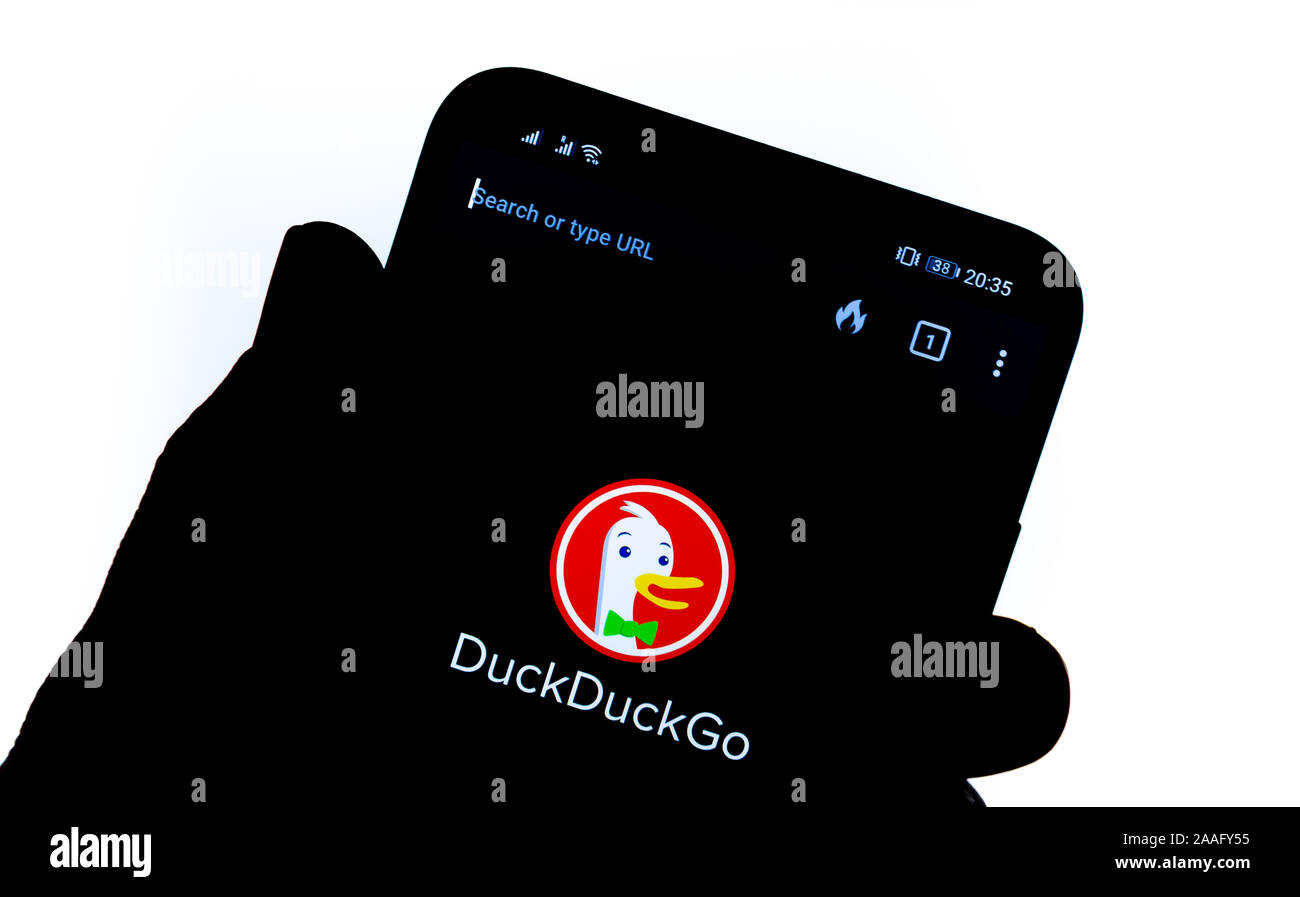 DuckDuckGo app on the smartphone screen hold by a silhouette of a hand. DuckDuckGo is an internet search engine focusing on user's privacy. Stock Photo